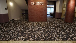 A hotel lobby with a patterned carpet, a reception desk, and a pillar with the hotel name.
