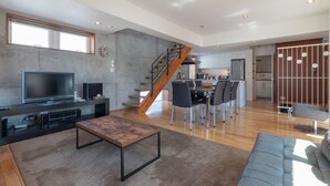 A modern living space with a flat-screen TV, a wooden coffee table, a sofa, a dining area with chairs, and a kitchen in the background. - Yuki Ten by H2 Life (Kutchan)