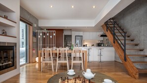 Un vaste espace de vie agrémenté d’un escalier en bois, d’une table à manger avec des chaises, d’une cheminée et d’un jeu d’échecs.
