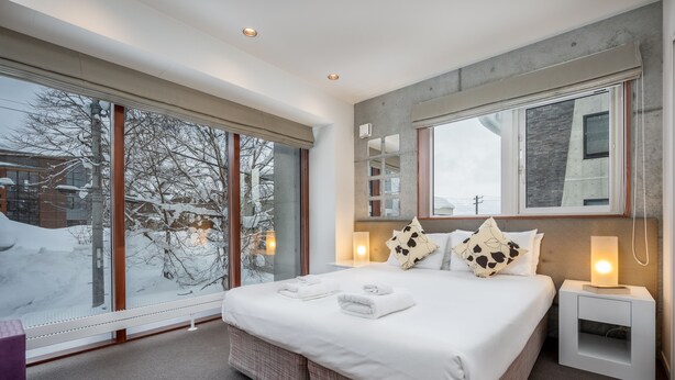 Une chambre d’hôtel moderne, dotée d’un grand lit, d’une table de chevet et d’une fenêtre donnant sur un paysage enneigé.