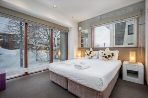 A modern hotel room with a large bed, a nightstand, and a window with a view of a snowy landscape.