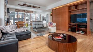 A modern living room with a sectional sofa, a round coffee table, a white armchair, and a built-in TV shelf. - Kitanishi 3 by H2 Life (Kutchan)