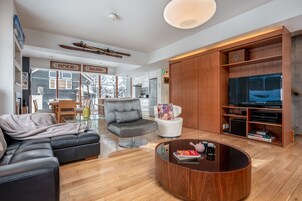 Una sala moderna con un sofá seccional, una mesa de centro redonda, un sillón blanco y un mueble empotrado para la televisión.