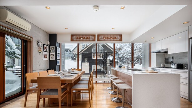 A modern kitchen with a central island, wooden dining table, and chairs. - Kitanishi 3 by H2 Life (Kutchan)