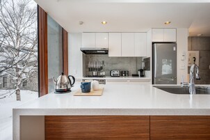 Una cocina moderna con armarios blancos, electrodomésticos de acero inoxidable y un amplio ventanal con vistas a un paisaje nevado.