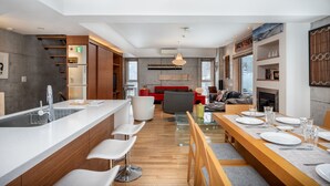 A modern kitchen with a central island, a dining area with a long wooden table, and a cozy living space with a red sofa and fireplace. - Kitanishi 3 by H2 Life (Kutchan)