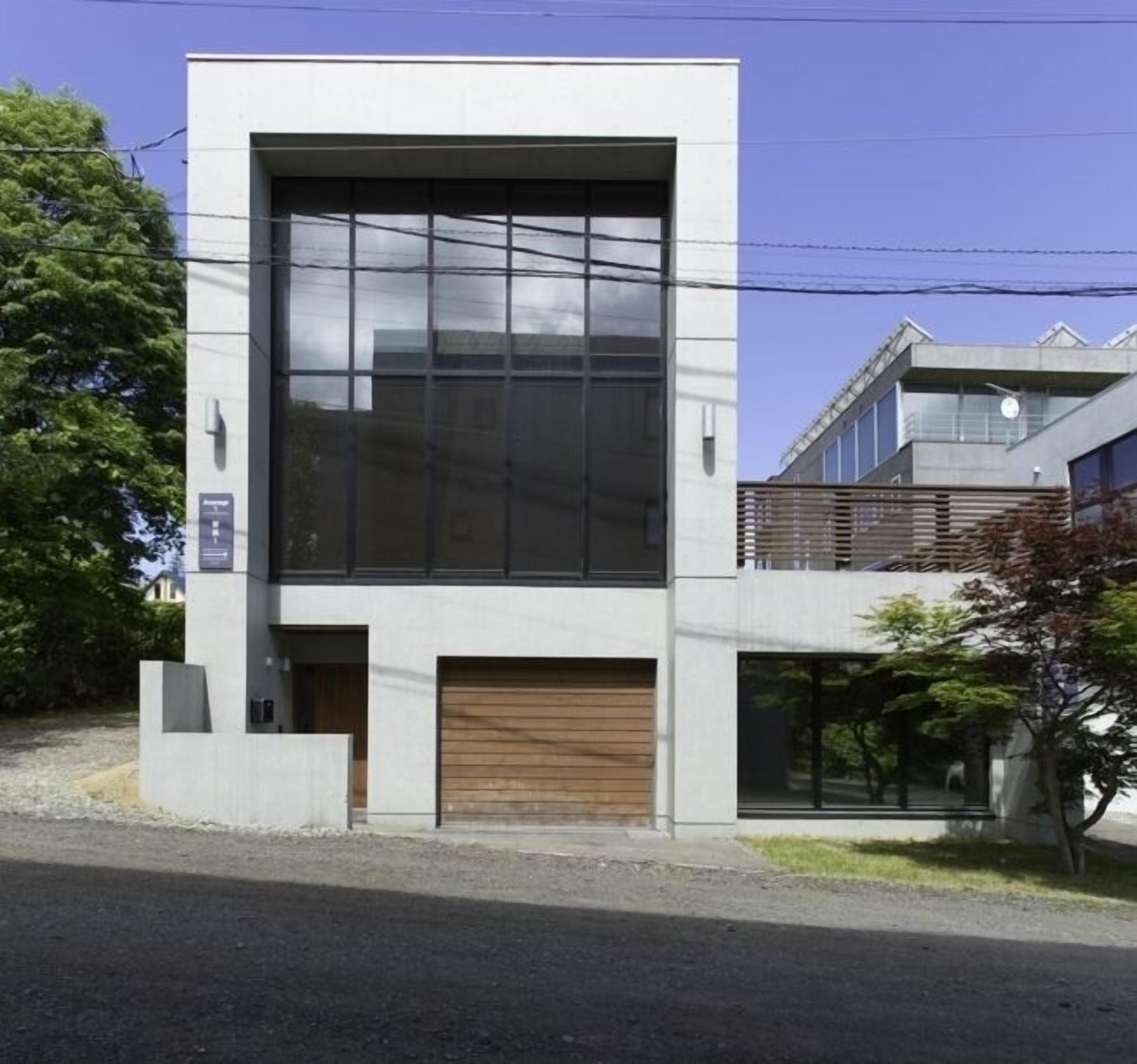 A modern building with a large glass facade, a wooden garage door, and a small entrance area. - Asanagi 3 bedroom by Hokkaido Tracks (Kutchan)