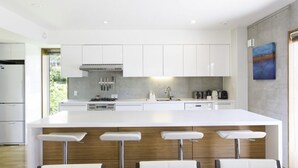 A modern kitchen with white cabinets, a central island with bar stools, and a view of the outdoors. - Asanagi 3 bedroom by Hokkaido Tracks (Kutchan)