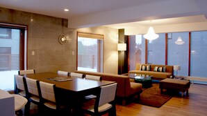 A modern living room with a dining area, large windows, and a sofa with cushions. - Asanagi 3 bedroom by Hokkaido Tracks (Kutchan)
