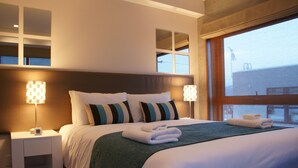 A neatly made bed with pillows, a bedside table with a lamp, and a window with a view of the outside. - Asanagi 3 bedroom by Hokkaido Tracks (Kutchan)