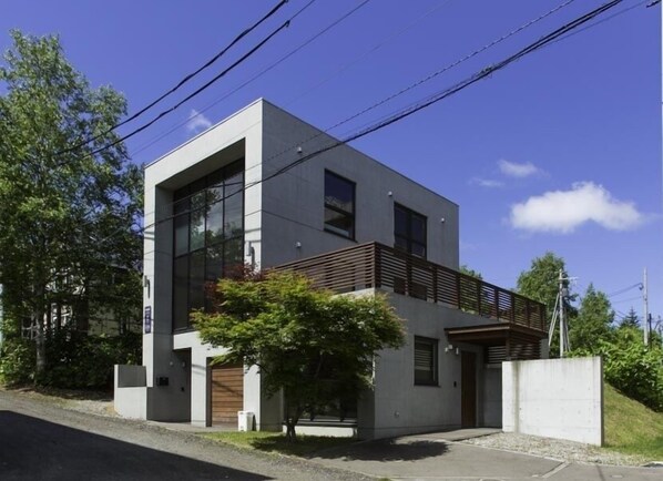 A modern two-story building with large windows, a flat roof, and a small balcony.