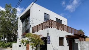 Um edifício moderno de dois andares com telhado plano, grandes janelas e varanda com ripas de madeira.