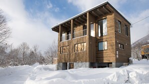 Ein modernes, zweistöckiges Holzhaus mit großen Fenstern und einem Balkon, umgeben von Schnee.
