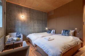 Een moderne hotelkamer met twee bedden, een klein tafeltje met een stoel en een houten plafond.