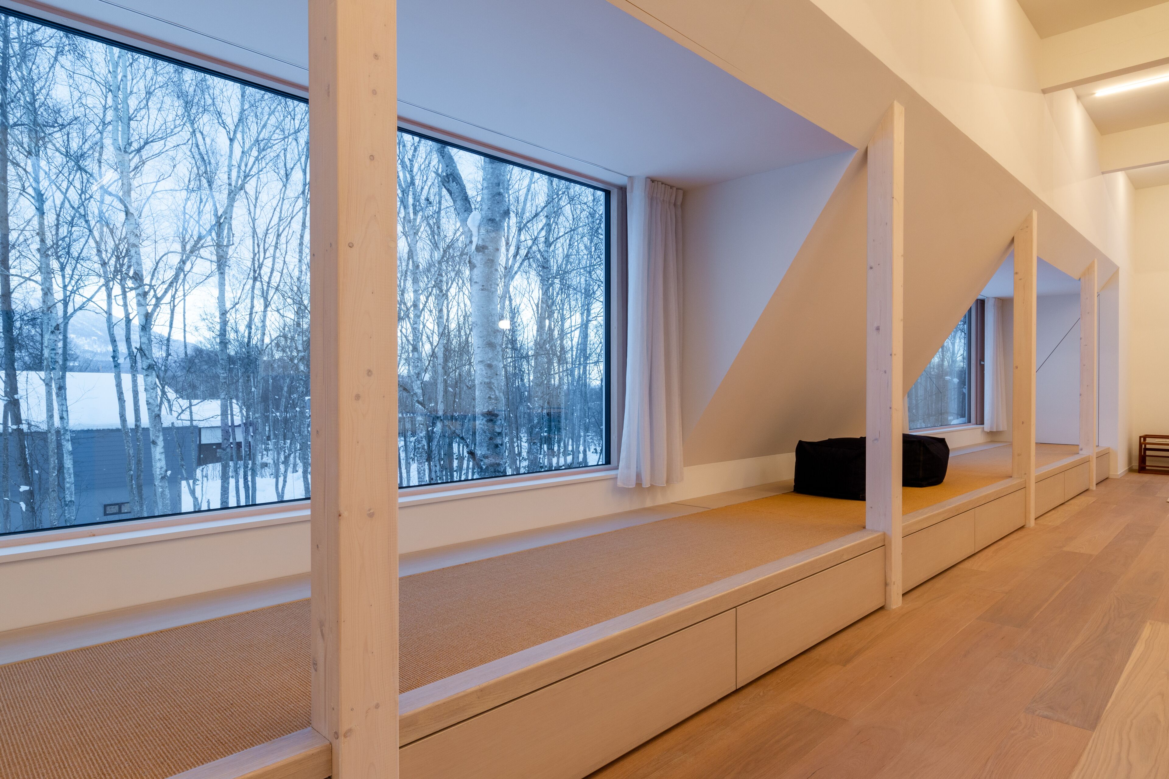 A modern interior with large windows, wooden beams, and a built-in bench along the wall.