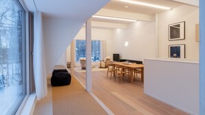 A modern interior with a dining area, a large window, and a view of trees. - Chalet W by H2 Life (Kutchan)