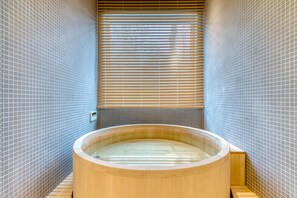 Una bañera de madera en una habitación con paredes de azulejos, una ventana y persianas.