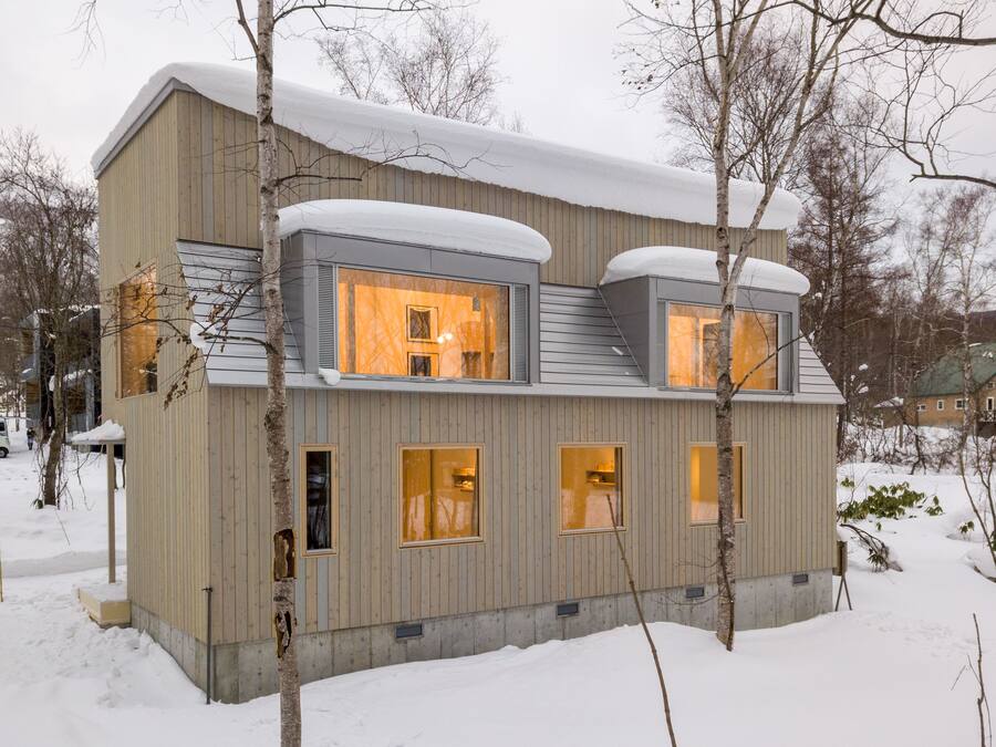 A modern, multi-story building with large windows and a sloped roof covered in snow.