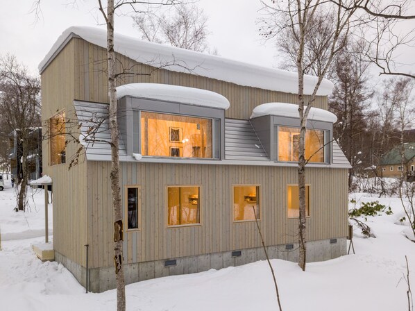 A modern, multi-story building with large windows and a sloped roof covered in snow.