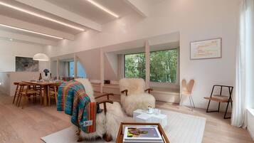 A modern interior with a dining area, a cozy seating area with a fireplace, and large windows offering a view of greenery.