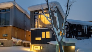 Un edificio moderno con fachada de madera, grandes ventanales y un balcón visible. Hay nieve alrededor de la estructura.