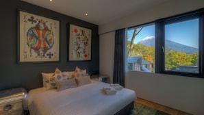 Habitación de hotel moderna con una cama grande, dos cuadros en la pared, vista a una montaña y una ventana con cortinas.