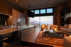A modern living room with a large window, a dining area with a wooden table, and a sofa. - Odile by Hokkaido Tracks (Kutchan)