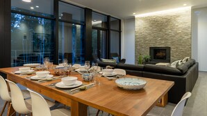 A modern dining area with a wooden table set for a meal, large windows, and a stone wall with a fireplace.
