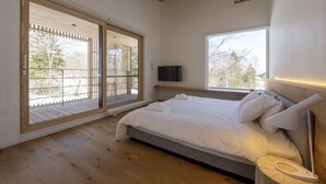 A bedroom with a bed, a TV, and large windows.