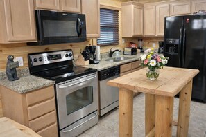 A modern kitchen with stainless steel appliances, wooden cabinets, a granite countertop, and a wooden table with a vase of flowers. - All the amenities you need for R&R and/or fun, can sleep 18, Game Room. (gatlinburg)
