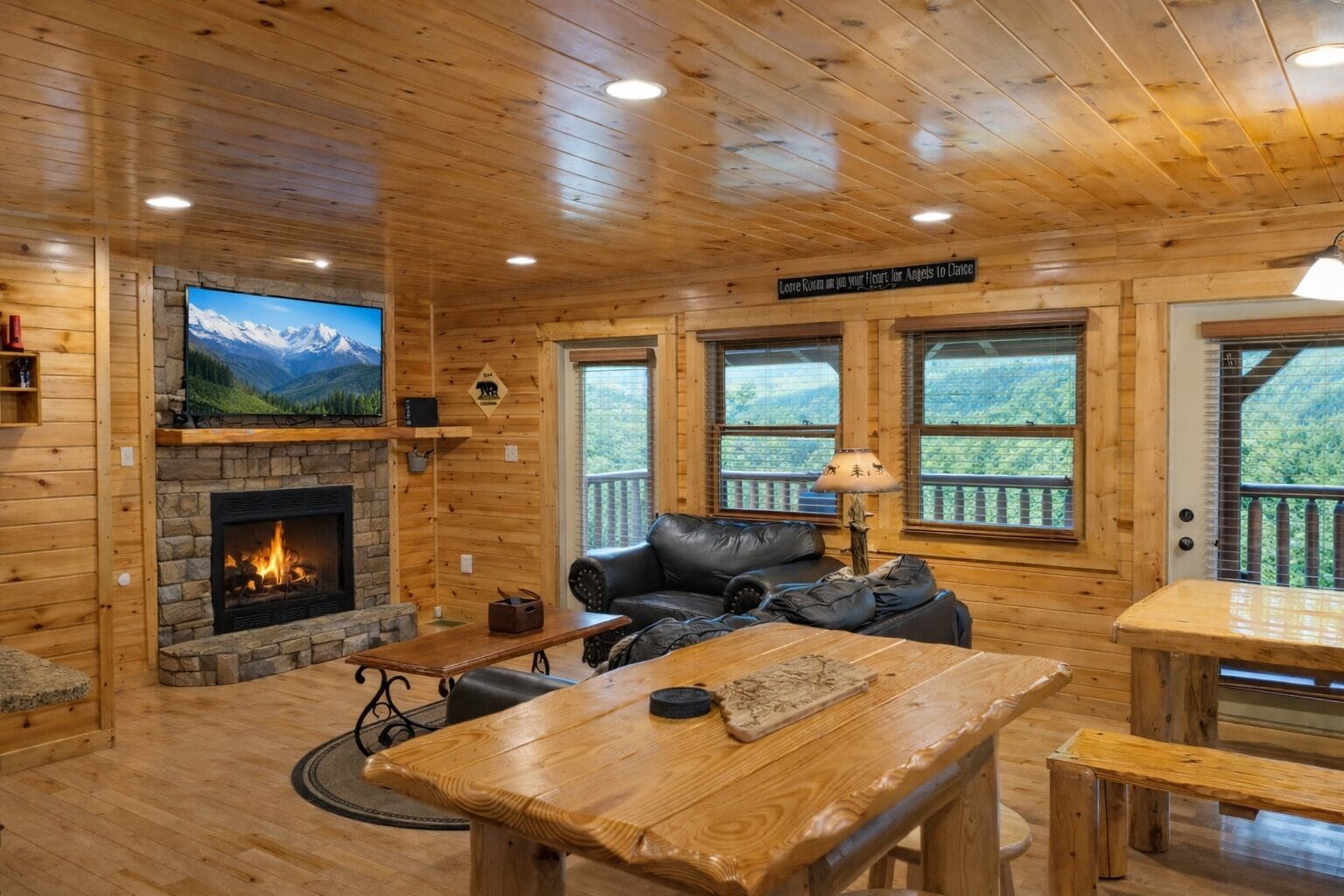 Ein gemütliches Cabin-Interieur mit Kamin aus Stein, Ledersofa, Esstisch aus Holz und großen Fenstern mit Blick auf die Berge.