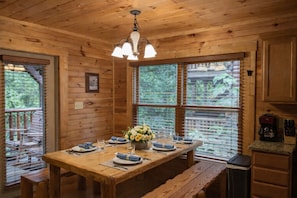 A wooden cabin interior with a dining table set for four, a chandelier, and large windows with blinds. - All the amenities you need for R&R and/or fun, can sleep 18, Game Room. (gatlinburg)