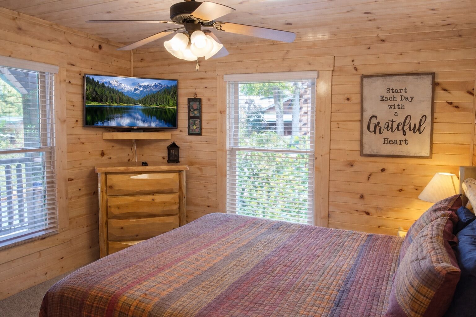 A cozy cabin room with a bed, dresser, TV, and a motivational quote on the wall.