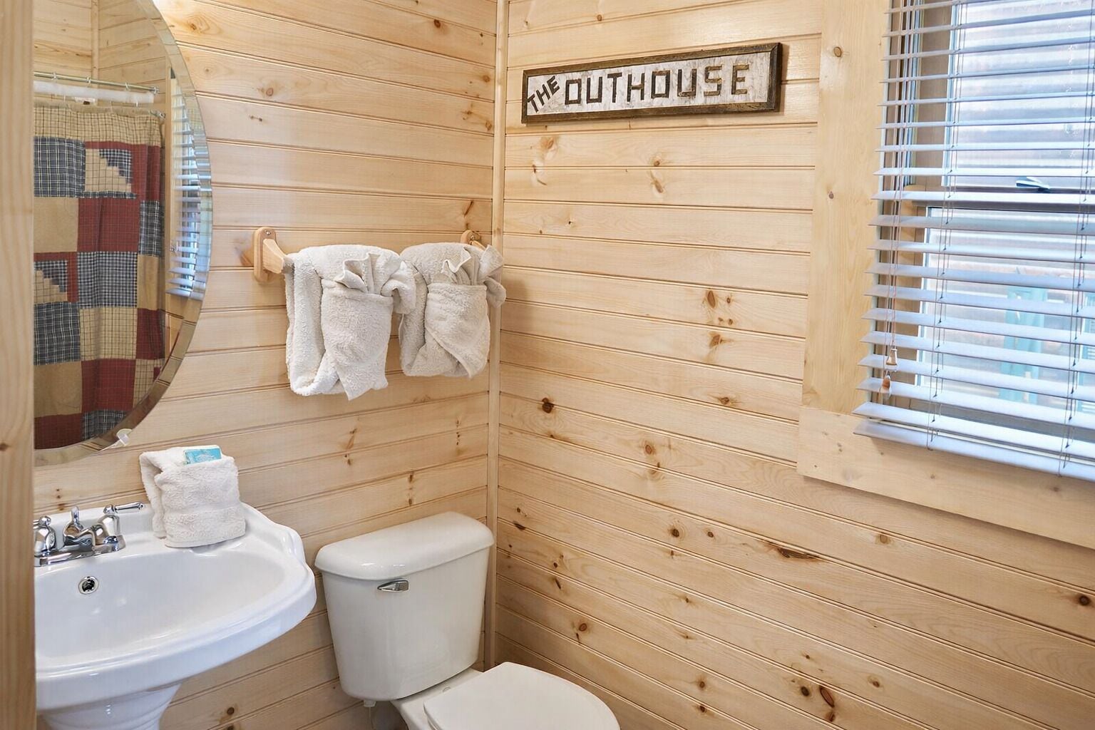 A wooden cabin bathroom with a sink, toilet, and a quilted mirror.