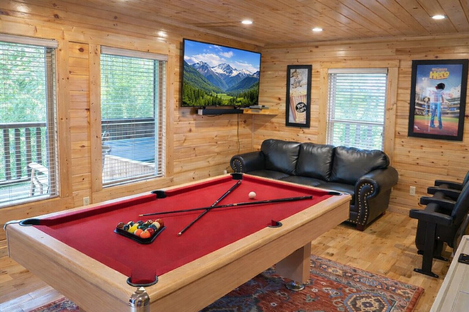 A pool table with balls, a leather sofa, and a mounted TV displaying a mountain landscape.