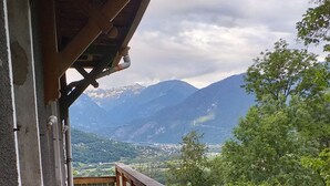 Un balcón de madera con barandilla metálica que da a un paisaje montañoso.