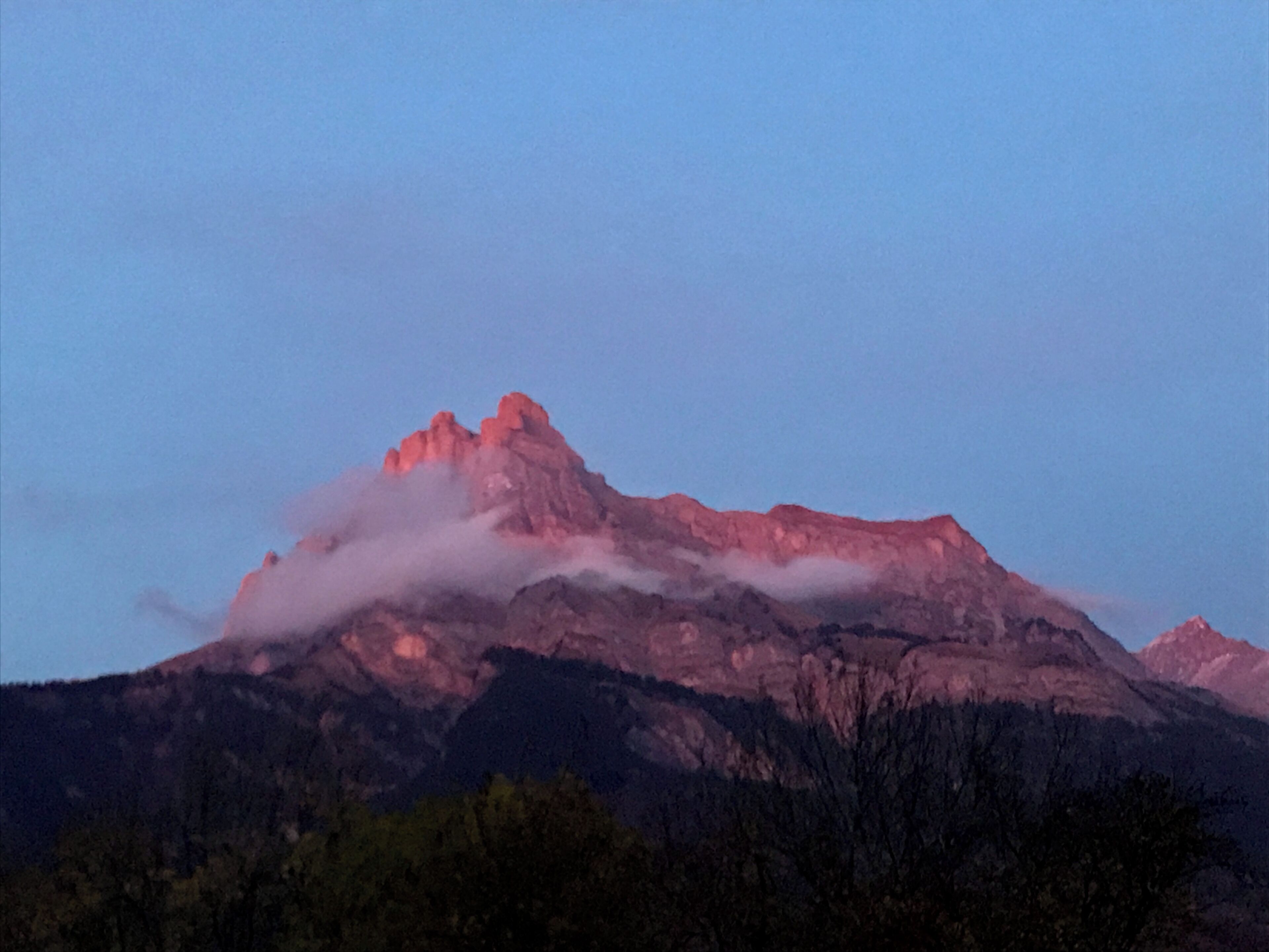 Ein Berg mit einem markanten Gipfel, umgeben von bewaldeten Hügeln.