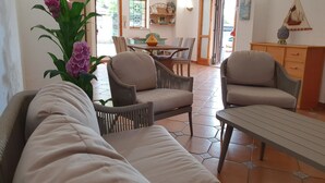 A living room with a sofa, two armchairs, a dining table with chairs, and a kitchen area in the background. - VILLA PLEMMYRIA. Semi-detached villa immersed in the greenery of the Plemmirio Marine Protected Oasis (Plemmirio)