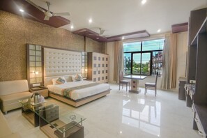 Quarto de hotel moderno com uma cama grande, uma mesa de centro de vidro, uma escrivaninha e vista para o exterior.