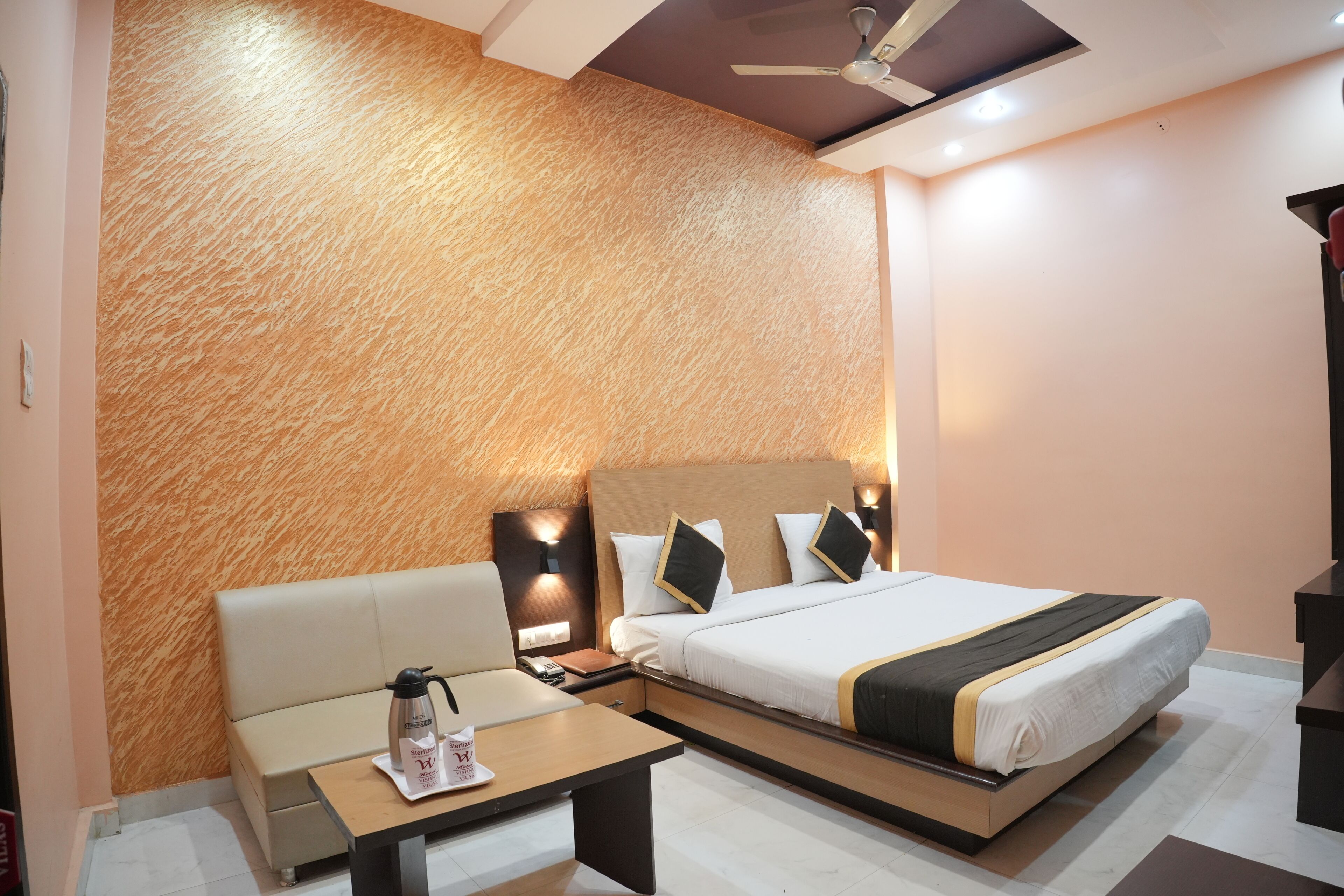 A hotel room with a bed, bedside table, lamp, and a sofa.