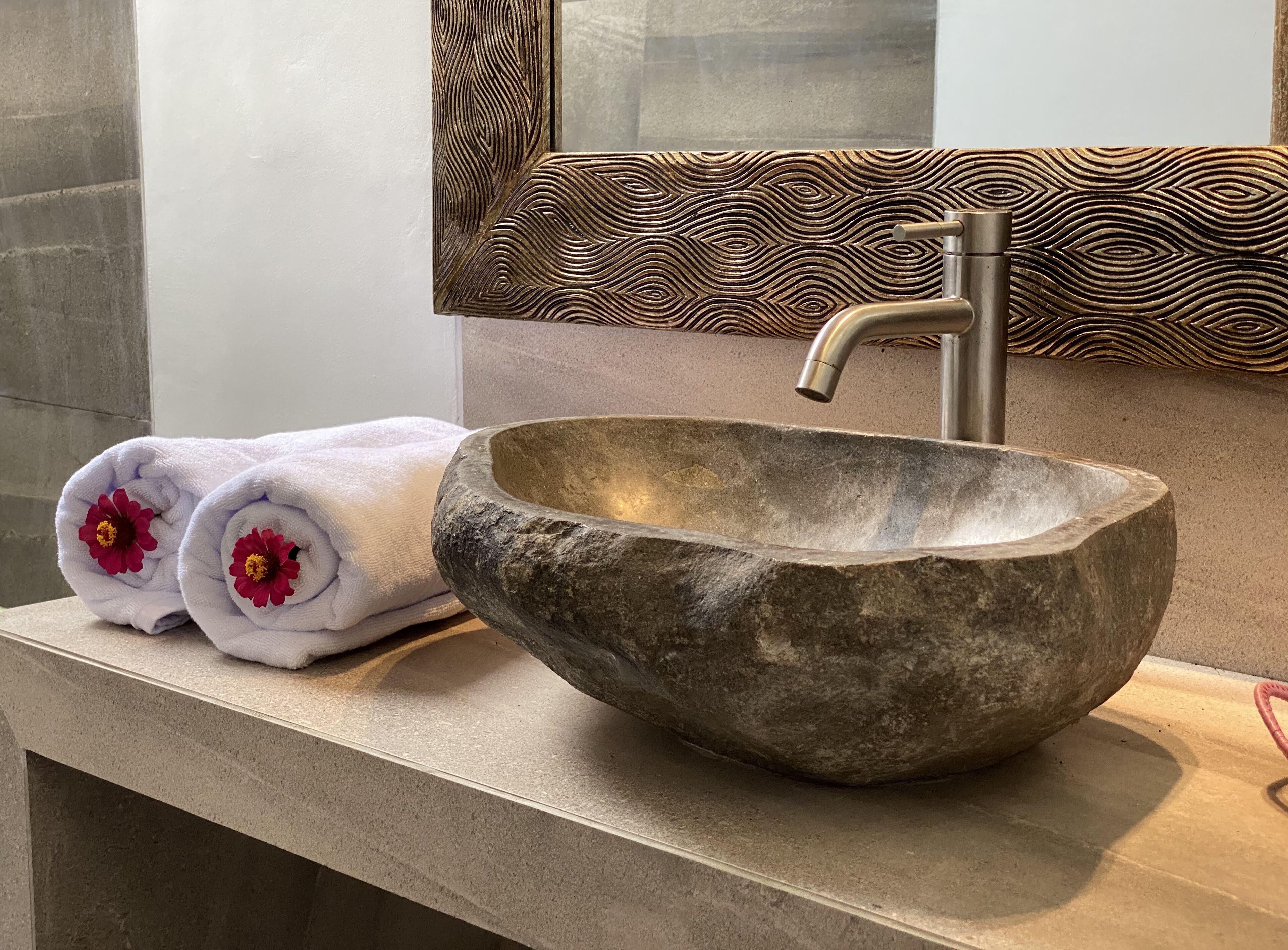 A stone sink with a modern faucet, a mirror with a textured backsplash, and two towels with red flowers.