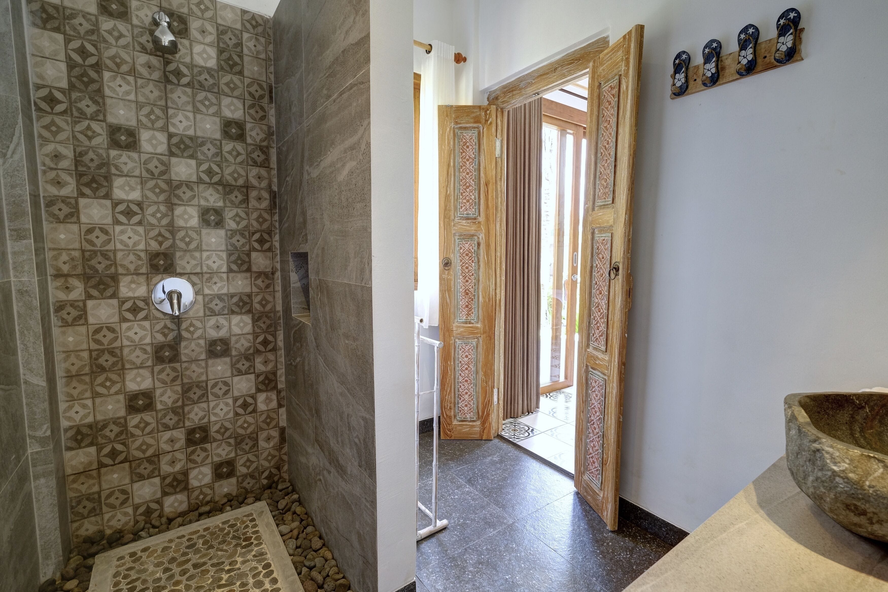 A bathroom with patterned tiles, a shower, a sink, and a decorative wooden door.