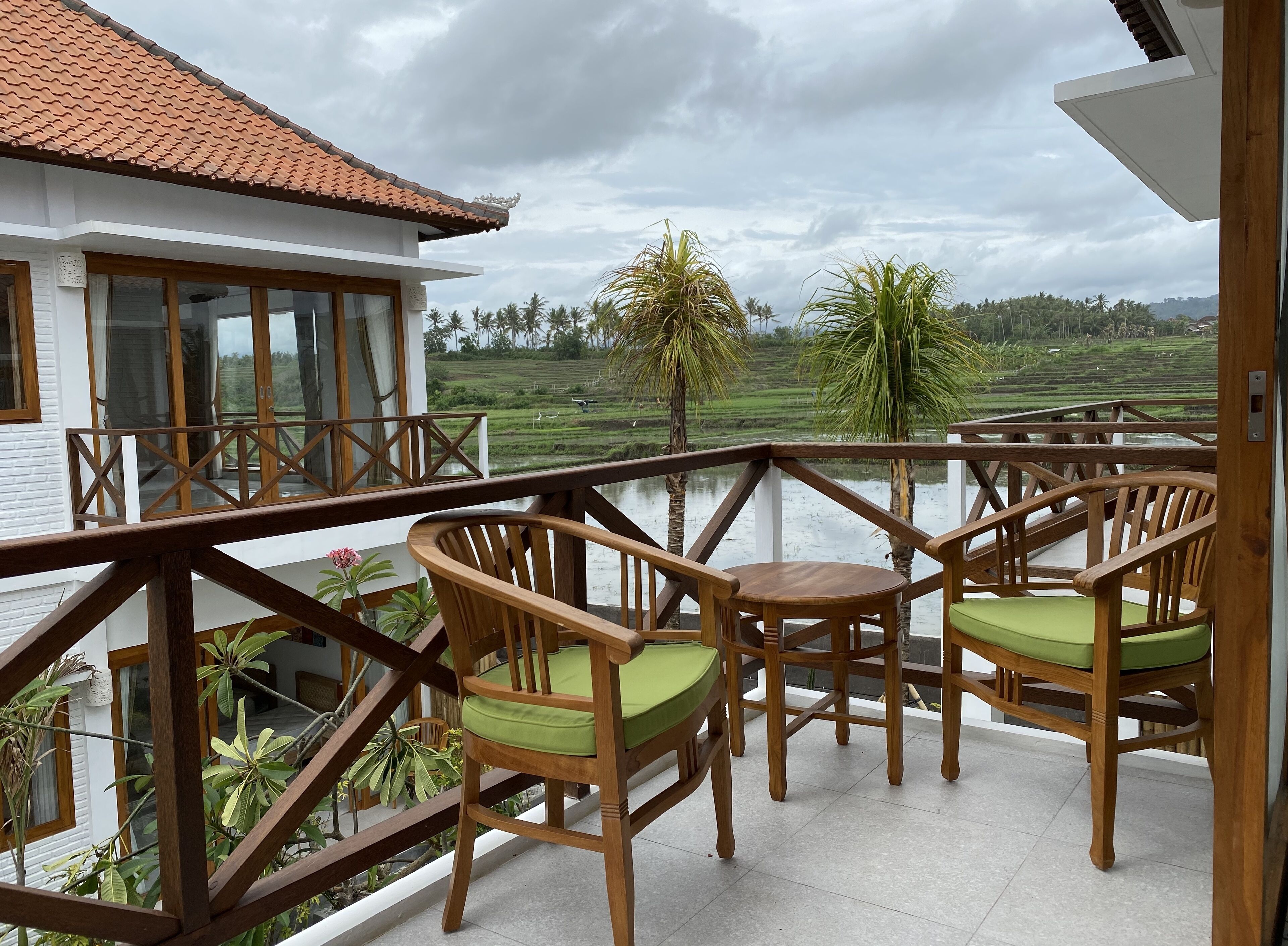 A balcony with wooden chairs and a view of a water body and green fields.