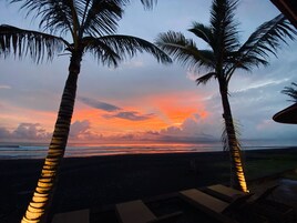 Vista del atardecer con palmeras y una playa.