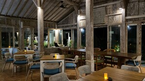 An indoor dining area with wooden tables and chairs, large windows, and a rustic ceiling. - Wide Sands Beach Retreat (Mendoyo)