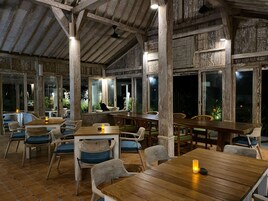 Un comedor interior con mesas y sillas de madera, ventanas amplias y un techo rústico.