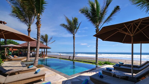 A poolside area with lounge chairs and umbrellas, overlooking a beach and ocean. - Wide Sands Beach Retreat (Mendoyo)