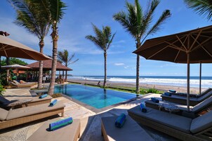 Zona junto a la piscina con sillas de descanso y sombrillas, con vista a una playa y al océano.