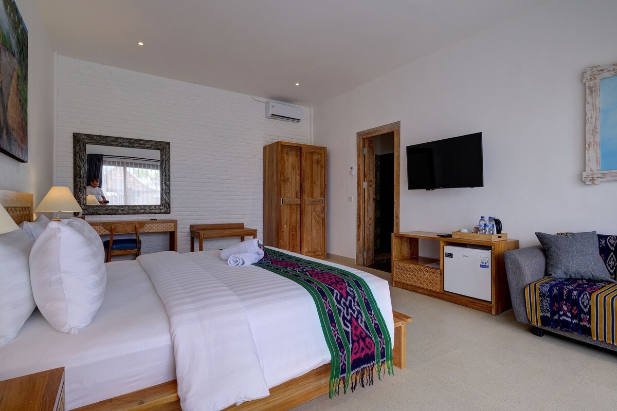A hotel room with a bed, a desk, a wardrobe, a television, and a sofa.