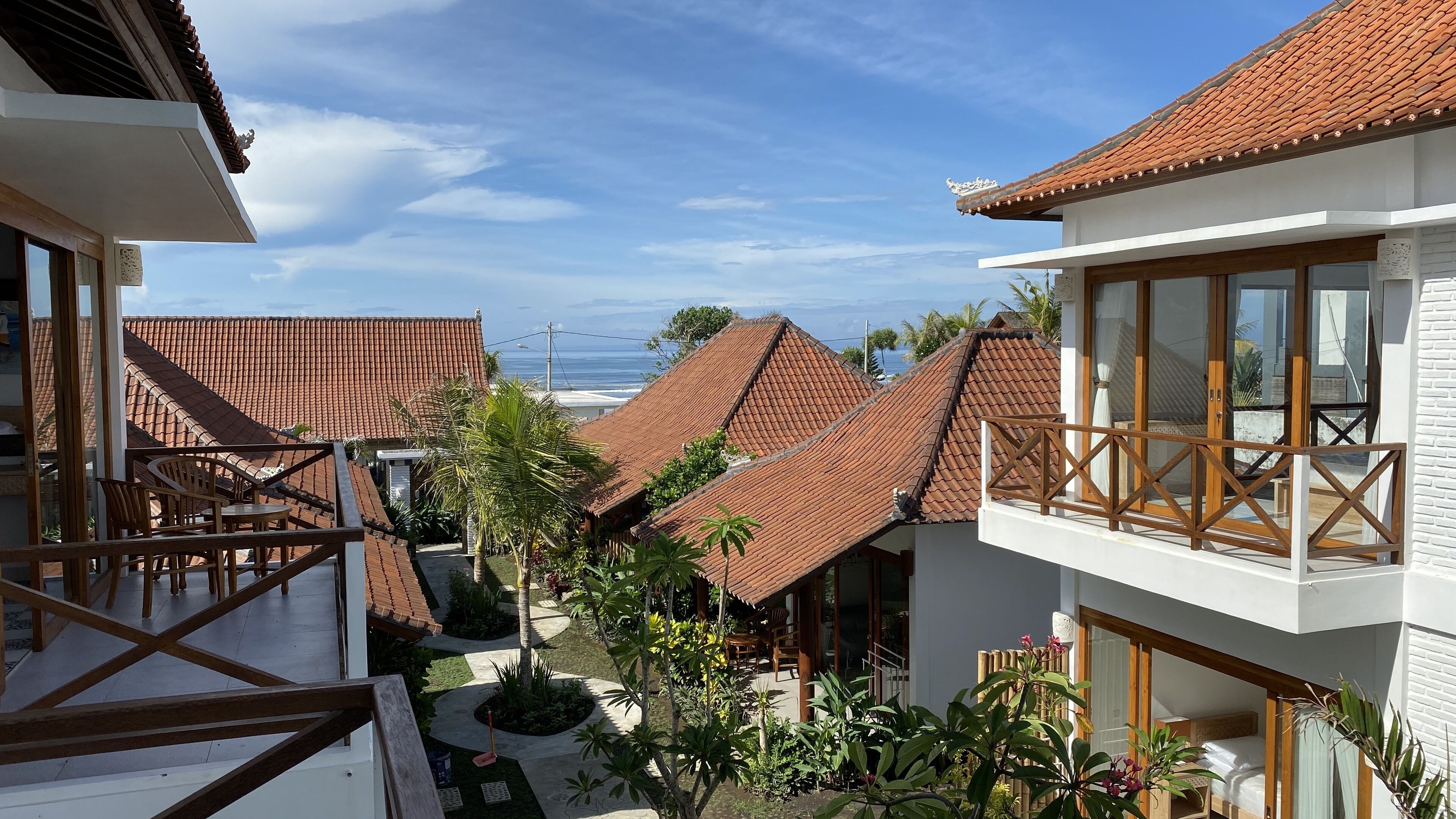 Een woonwijk met meerdere huizen, voorzien van rode dakpannen, een balkon met houten leuningen en uitzicht op de oceaan.